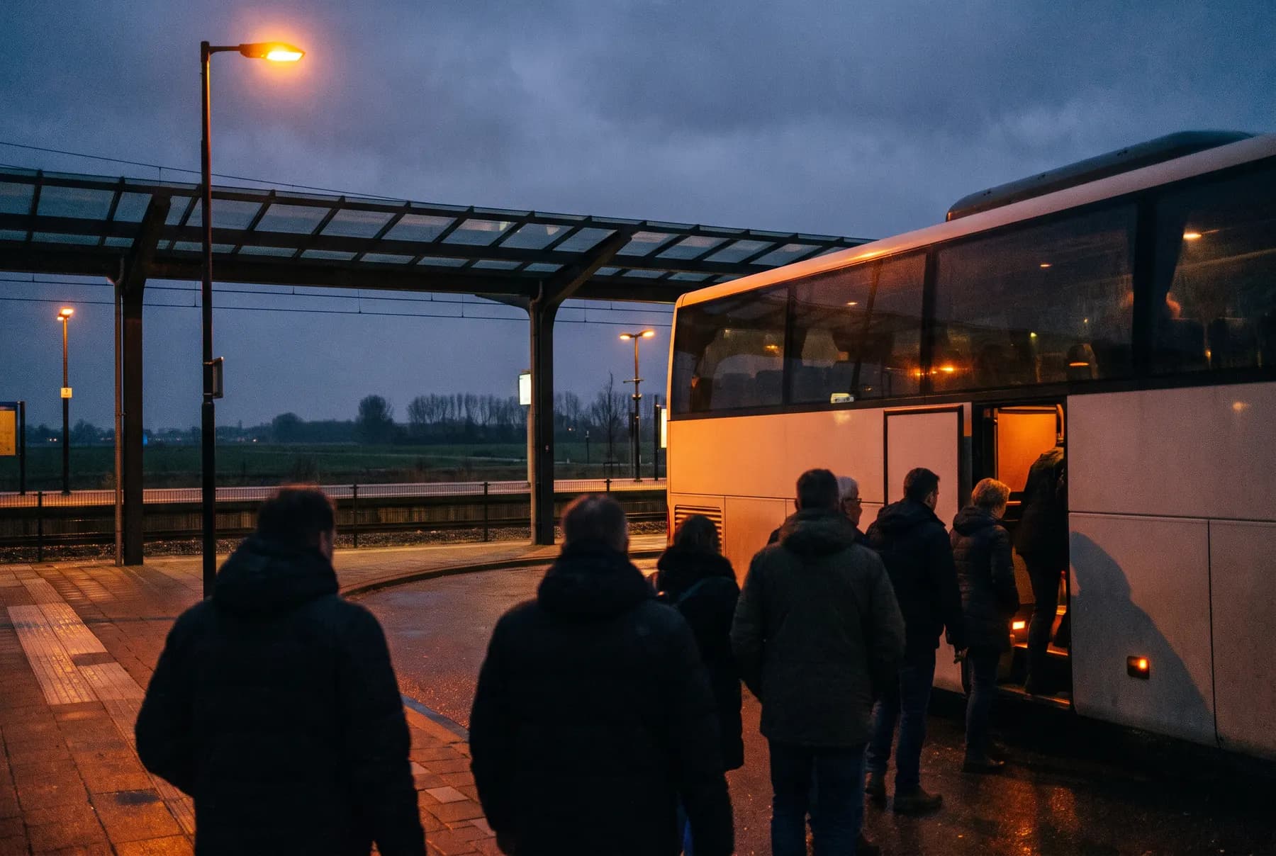 Festivalgangers stappen in de schemering bij een treinstation in een touringcar